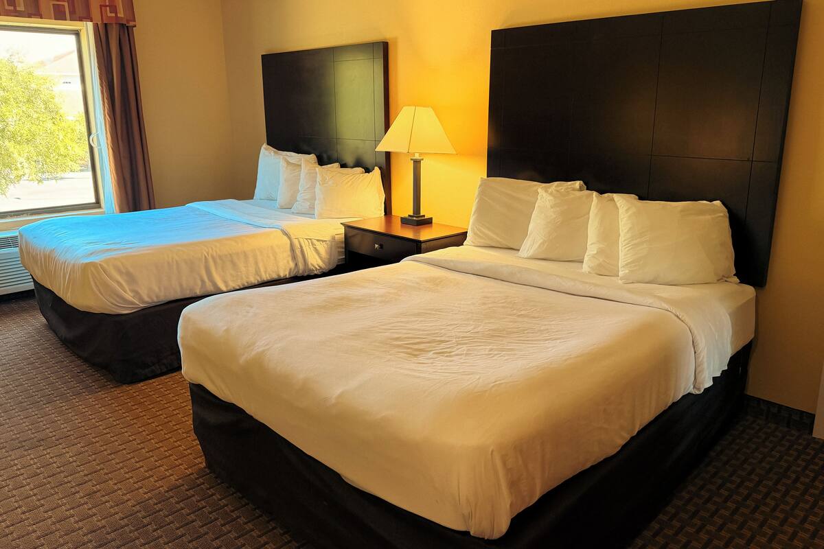 A hotel room with two beds, a nightstand with a lamp, and a window with curtains.