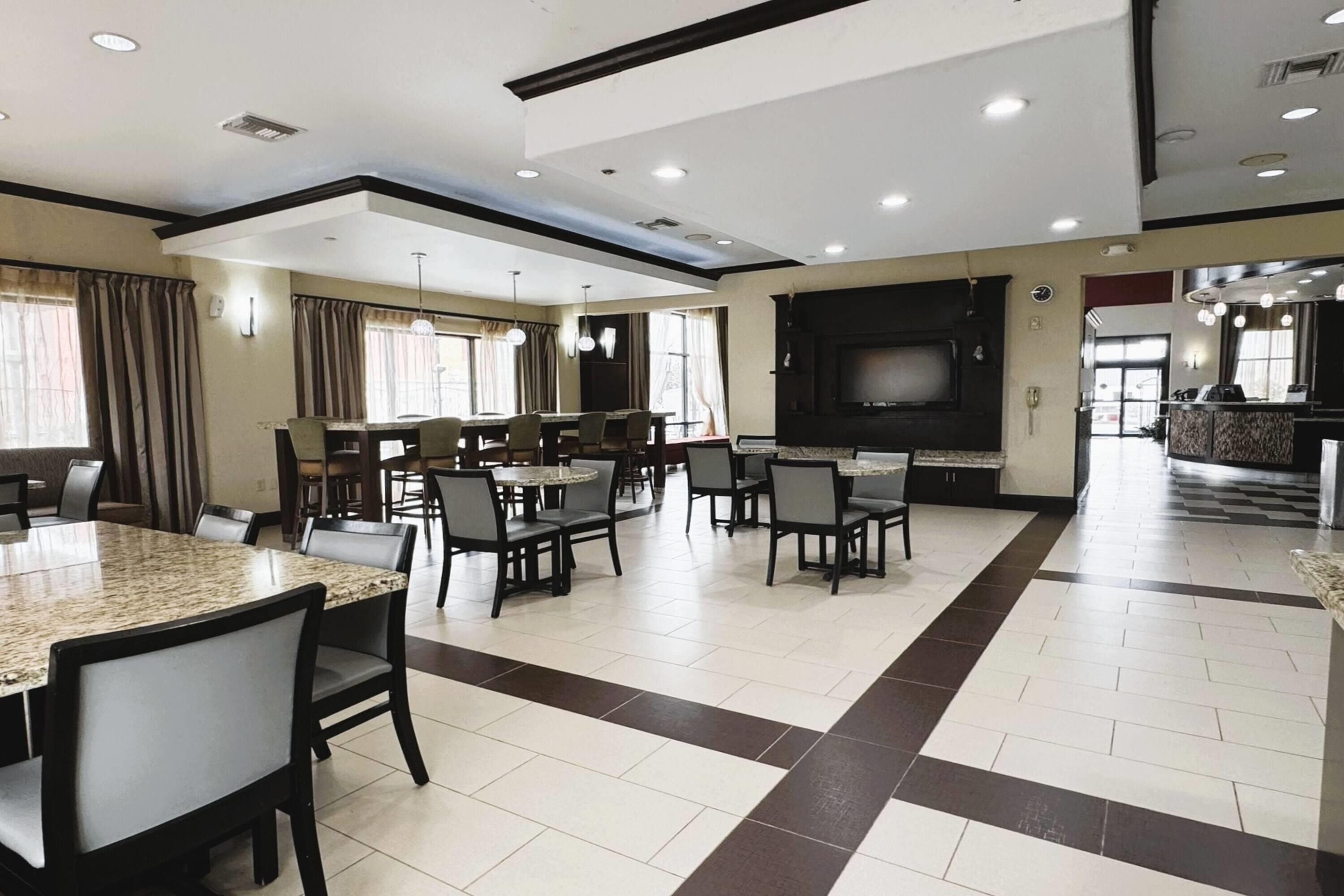 A spacious dining area with multiple tables and chairs, a large flat-screen TV, and a kitchen area in the background.
