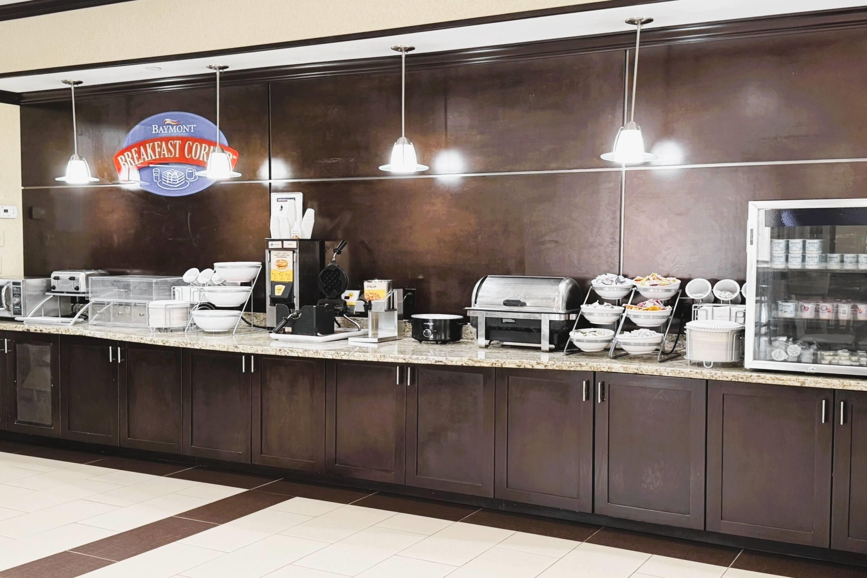 Mostrador de desayuno con un letrero de Baymont, máquinas de café, plancha y vitrina refrigerada.