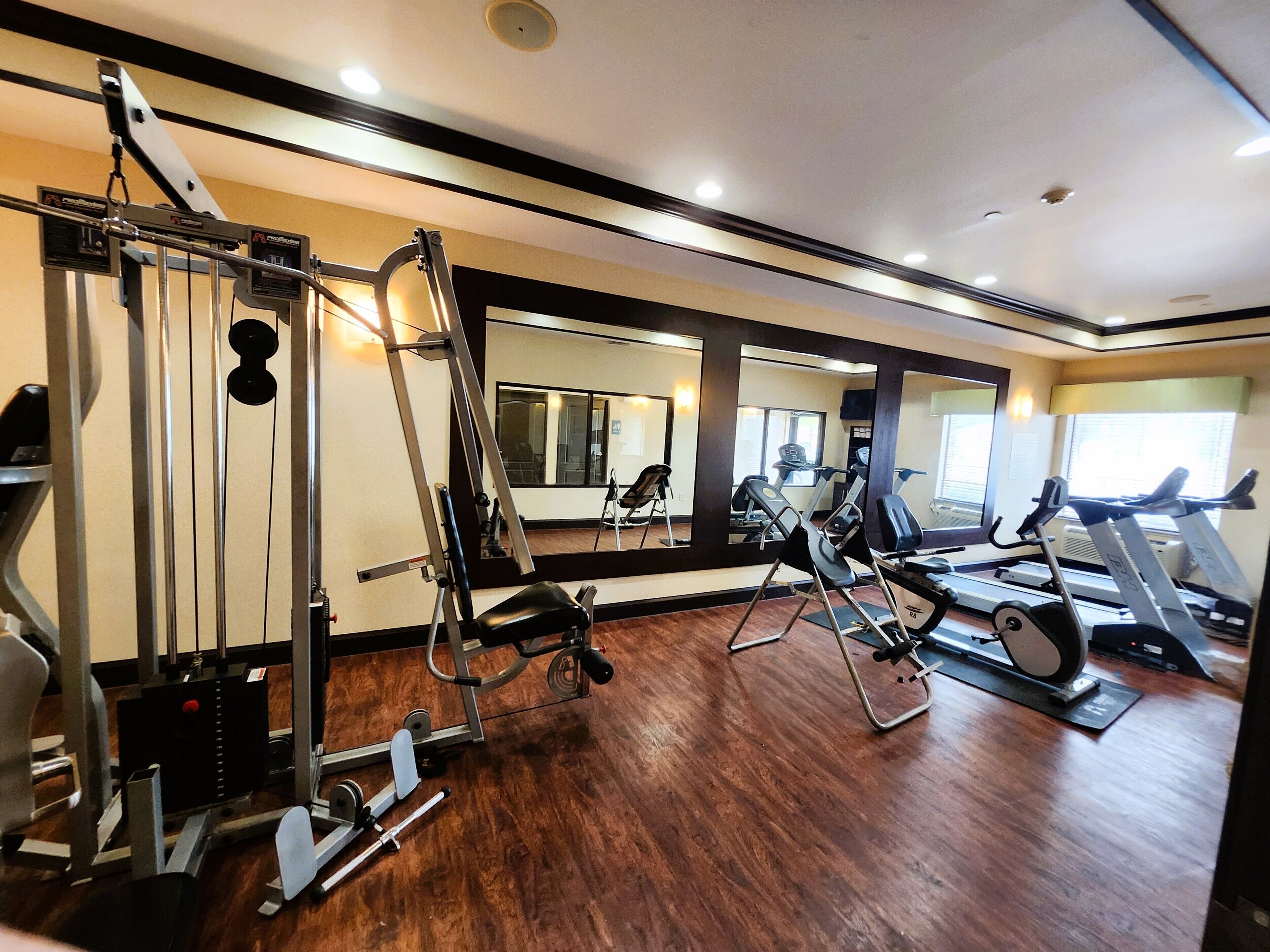 A gym with various exercise equipment, large mirrors, and a wooden floor.