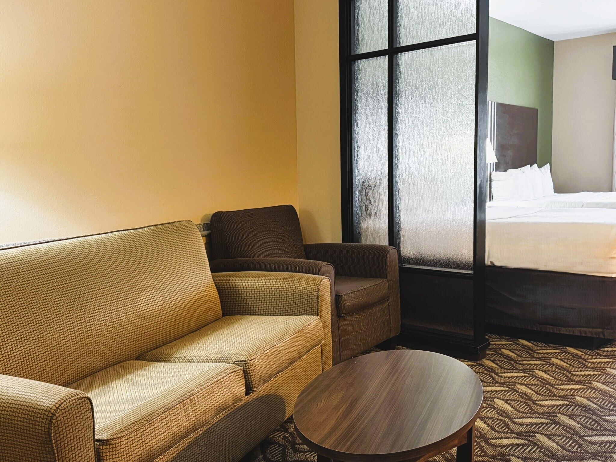 A hotel room with a sofa, armchair, and a round table.