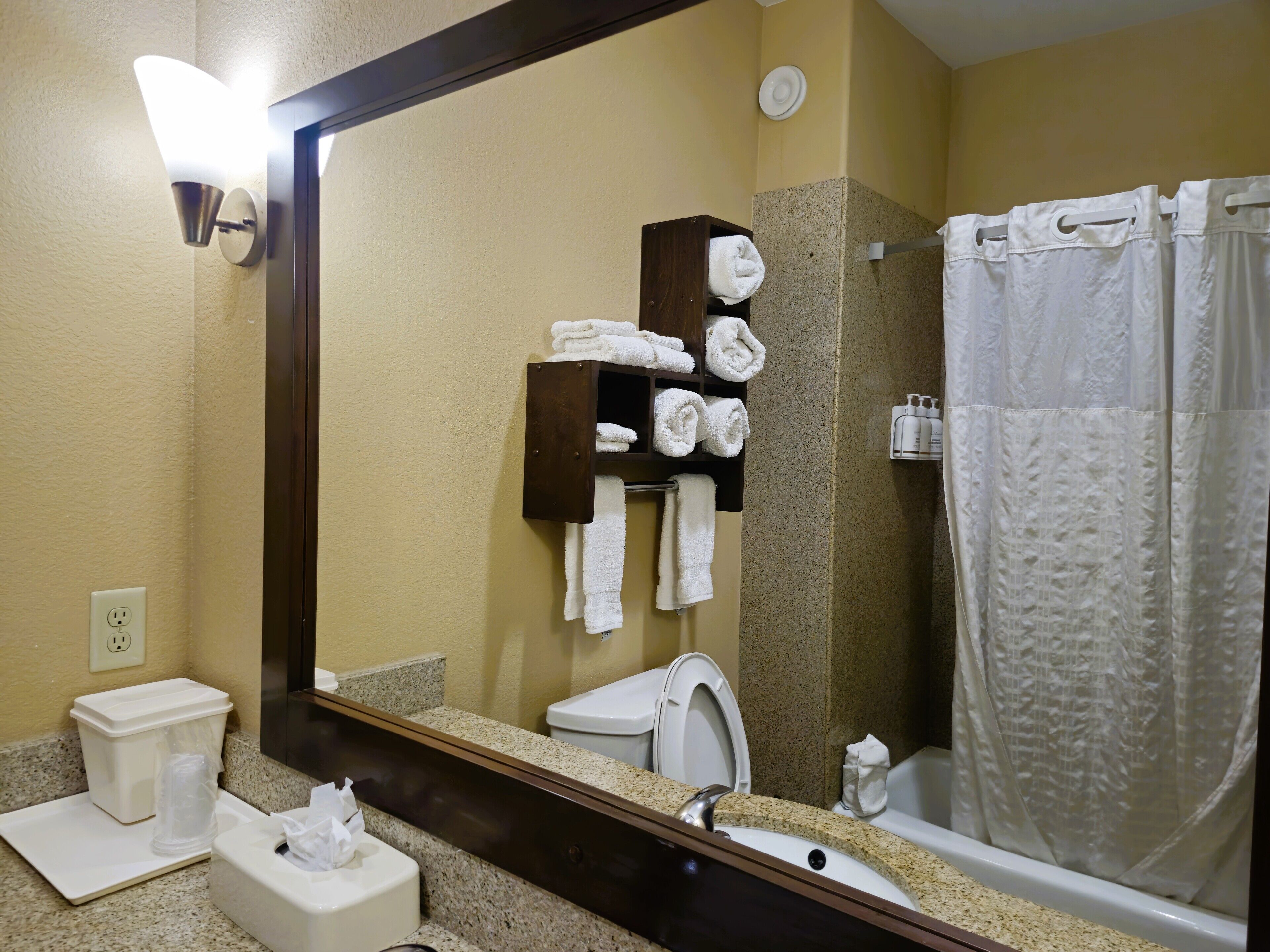 A bathroom with a sink, toilet, and shower. There is a towel rack with folded towels and a mirror.