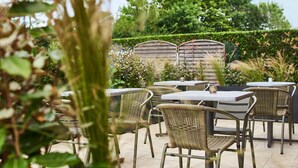 An outdoor patio area with wicker furniture and a stone wall in the background. - Kyriad Les Ulis (Les Ulis)