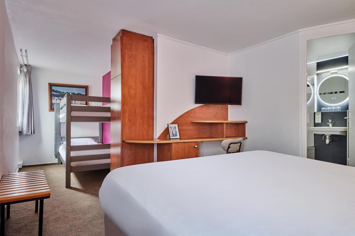 A hotel room with a bunk bed, a desk, a flat-screen TV, a vanity with a mirror, and a framed picture on the wall.