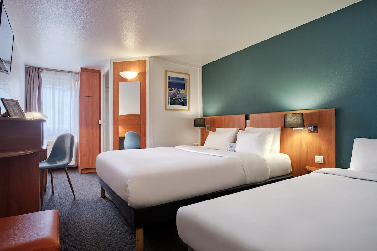 A hotel room with two beds, a desk, a chair, and a window with curtains.