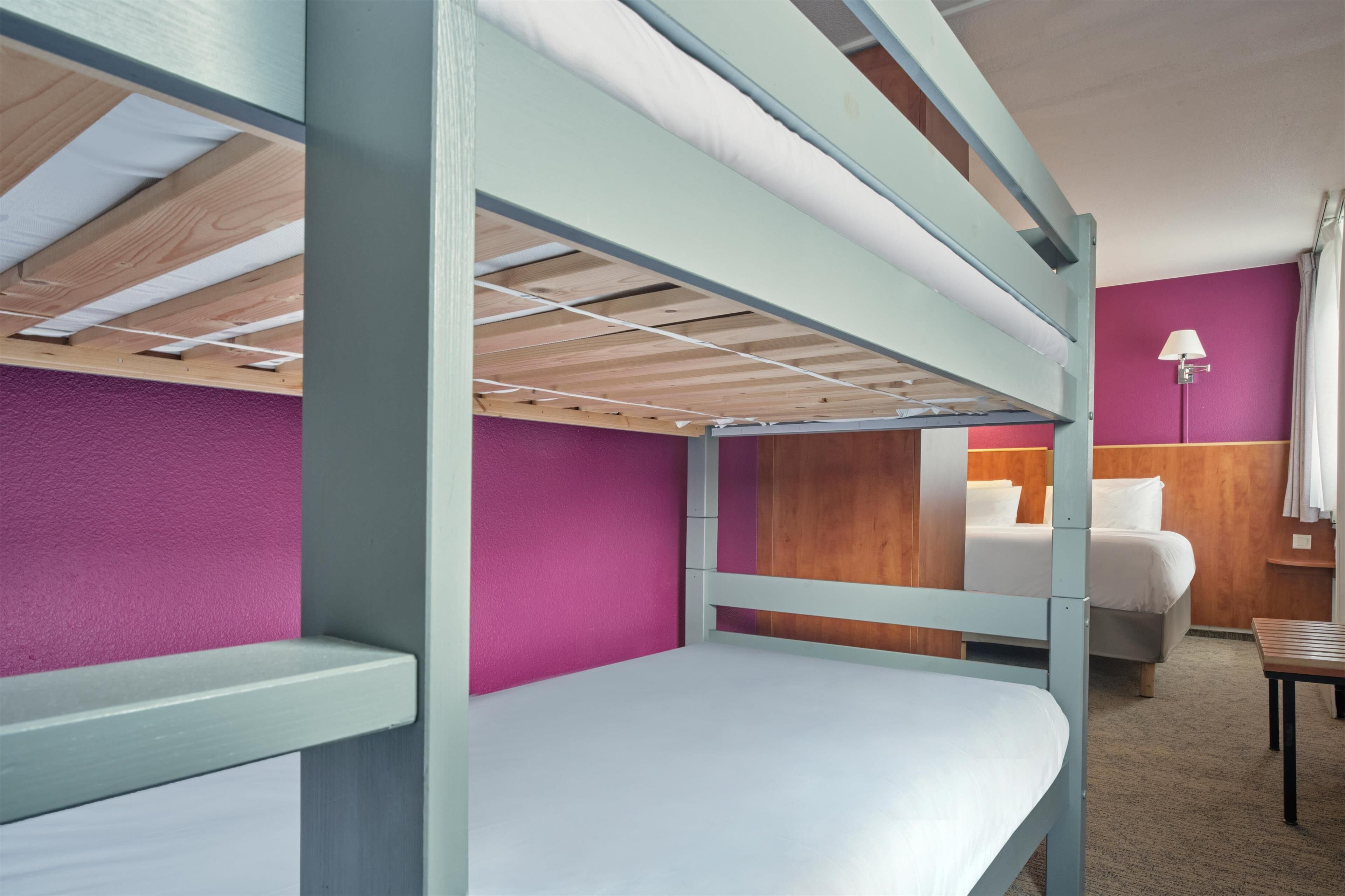 Dormitorio con literas, una pared morada, un cabecero de madera y una mesita de noche con lámpara.