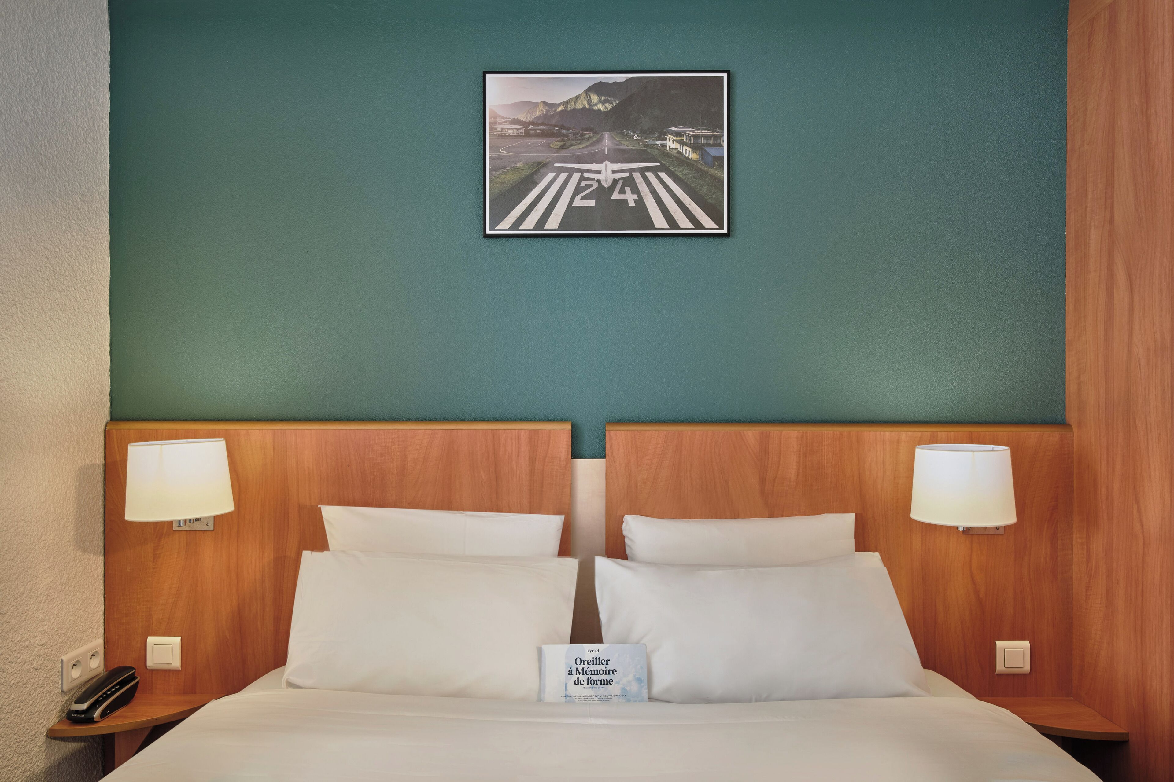A hotel room with a large bed, two bedside lamps, a nightstand with a phone, and a framed picture on the wall.