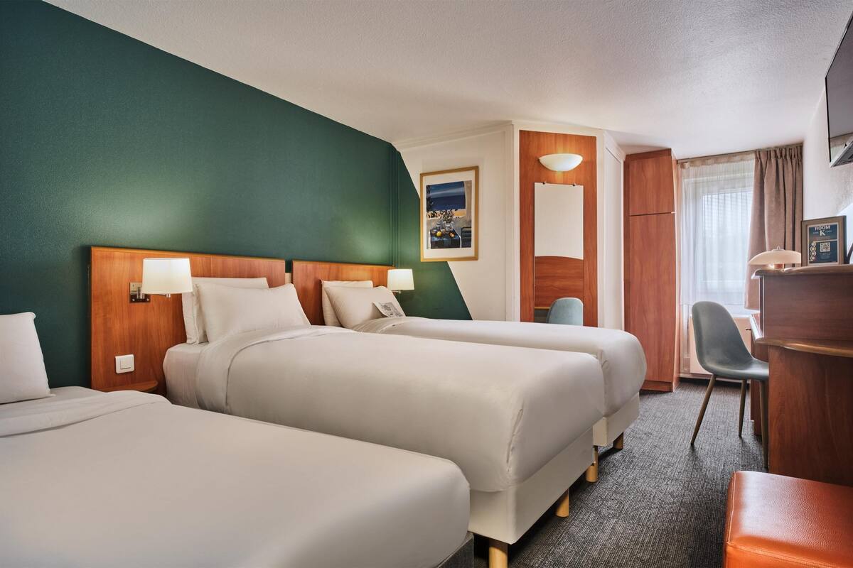 A hotel room with two beds, a desk, a chair, and a television.