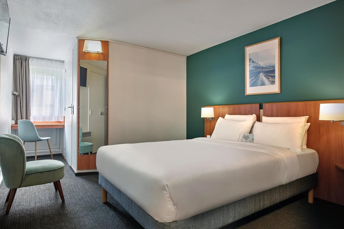 A hotel room with a large bed, a desk, a chair, and a painting on the wall.