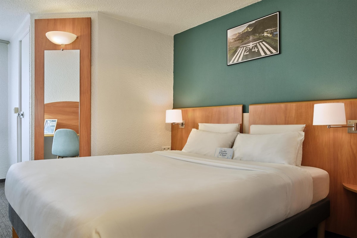A neatly made bed with white linens, a wooden headboard, and two bedside lamps.