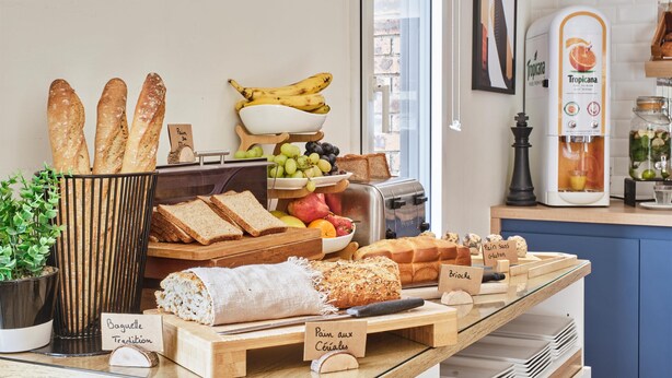 A bakery display with various breads, fruits, and a coffee machine. - Kyriad Les Ulis (Les Ulis)