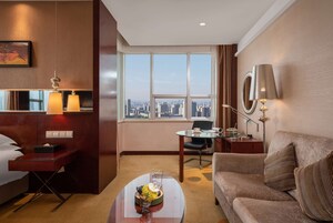 Habitación de hotel con vista a la ciudad, un sofá, una mesa de centro, un escritorio y una lámpara.