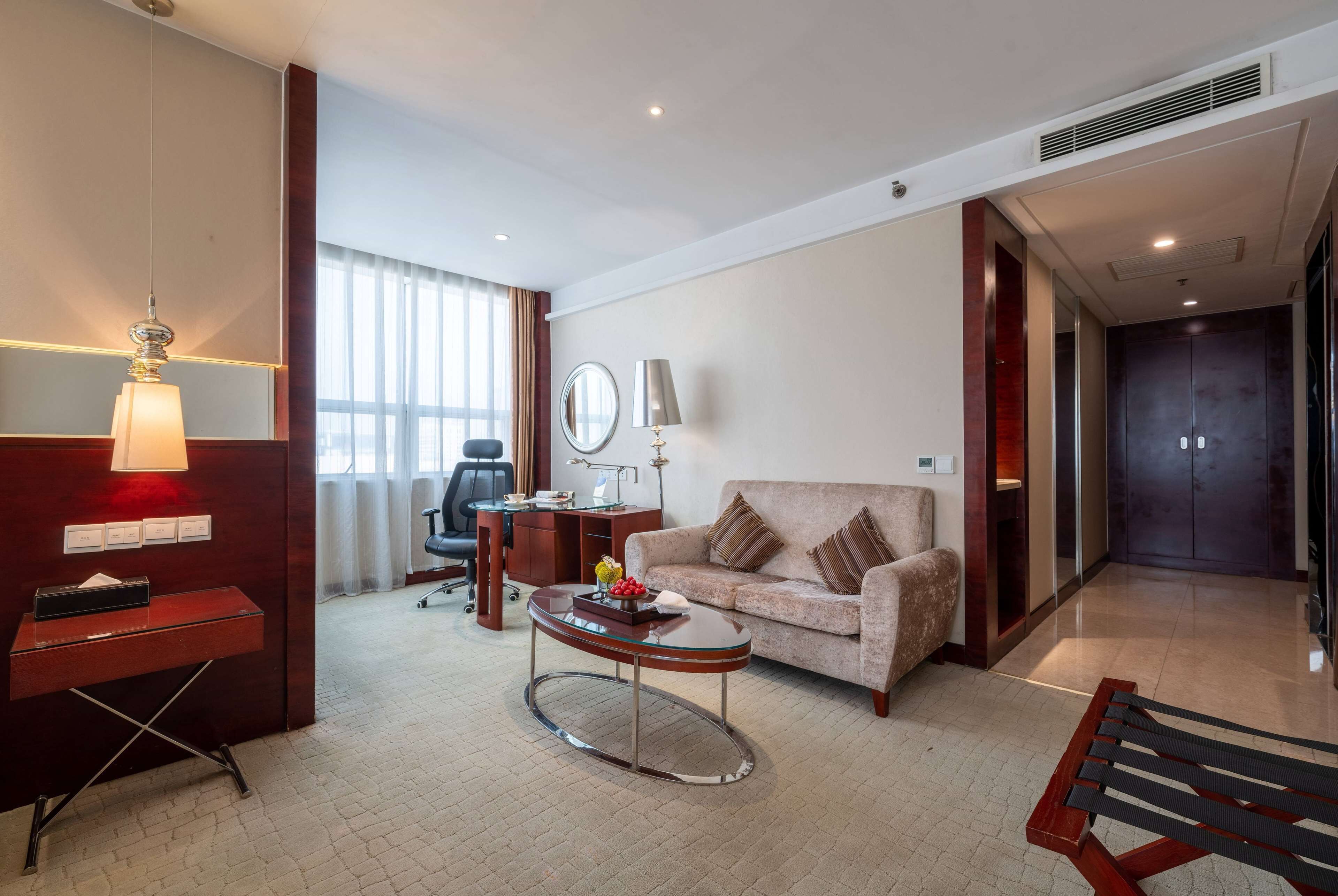 A hotel room with a wooden desk, a round coffee table, a sofa, and a large mirror.