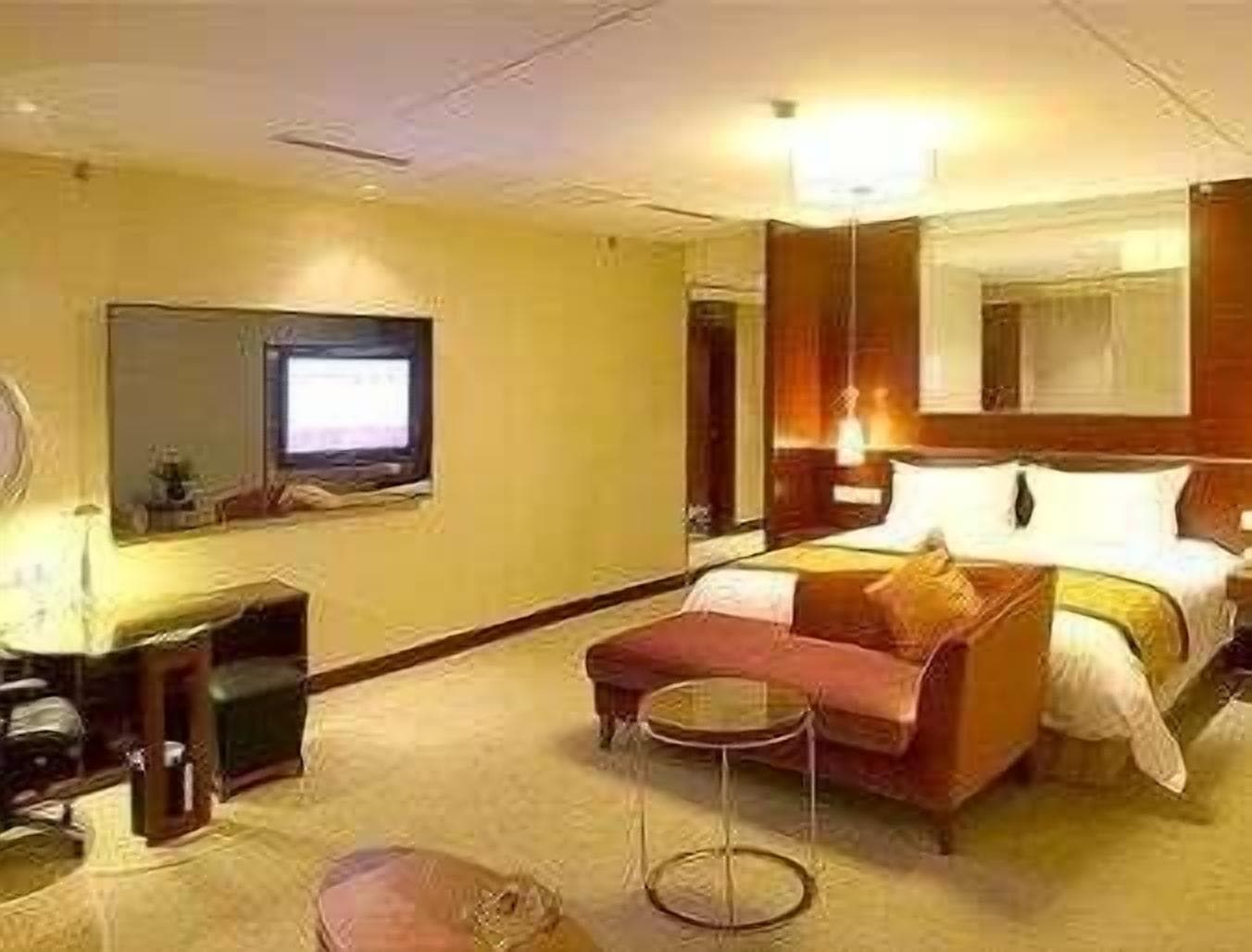 Ein Hotelzimmer mit einem Bett, einem kleinen Tisch, einer Couch, einem Fernseher und einem Spiegel.
