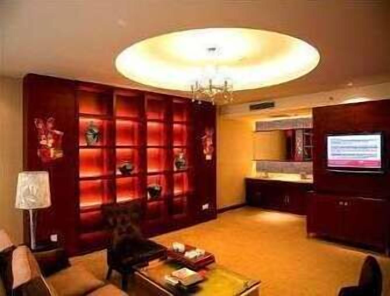 A modern living room with a large TV, a red bookshelf, and a chandelier.