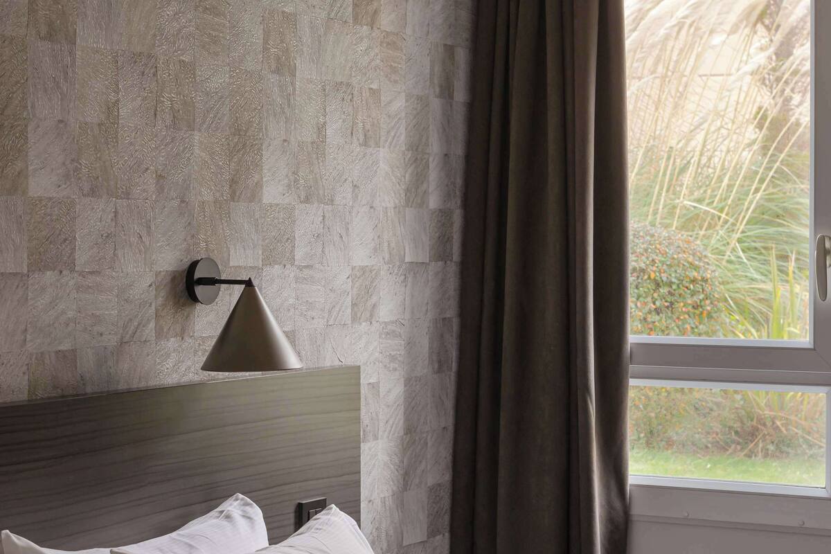 Hotelkamer met een bed, een wandlamp en een raam met gordijnen.