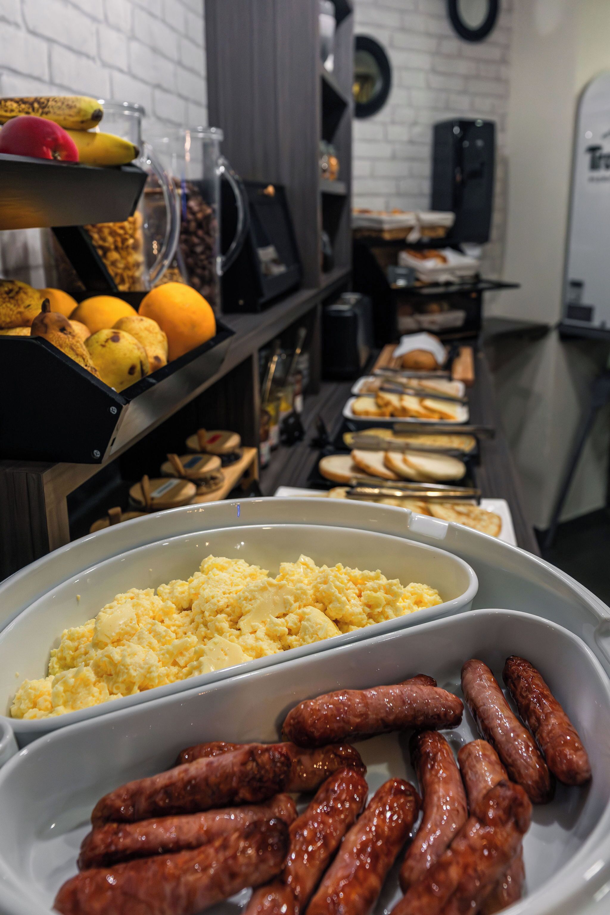 A buffet with various food items including sausages, scrambled eggs, and fruits.