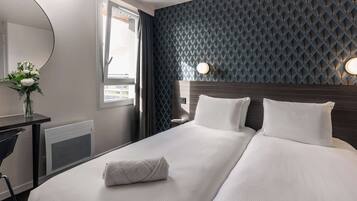 A hotel room with a large bed, a desk with a chair, a mirror, and a window with curtains.