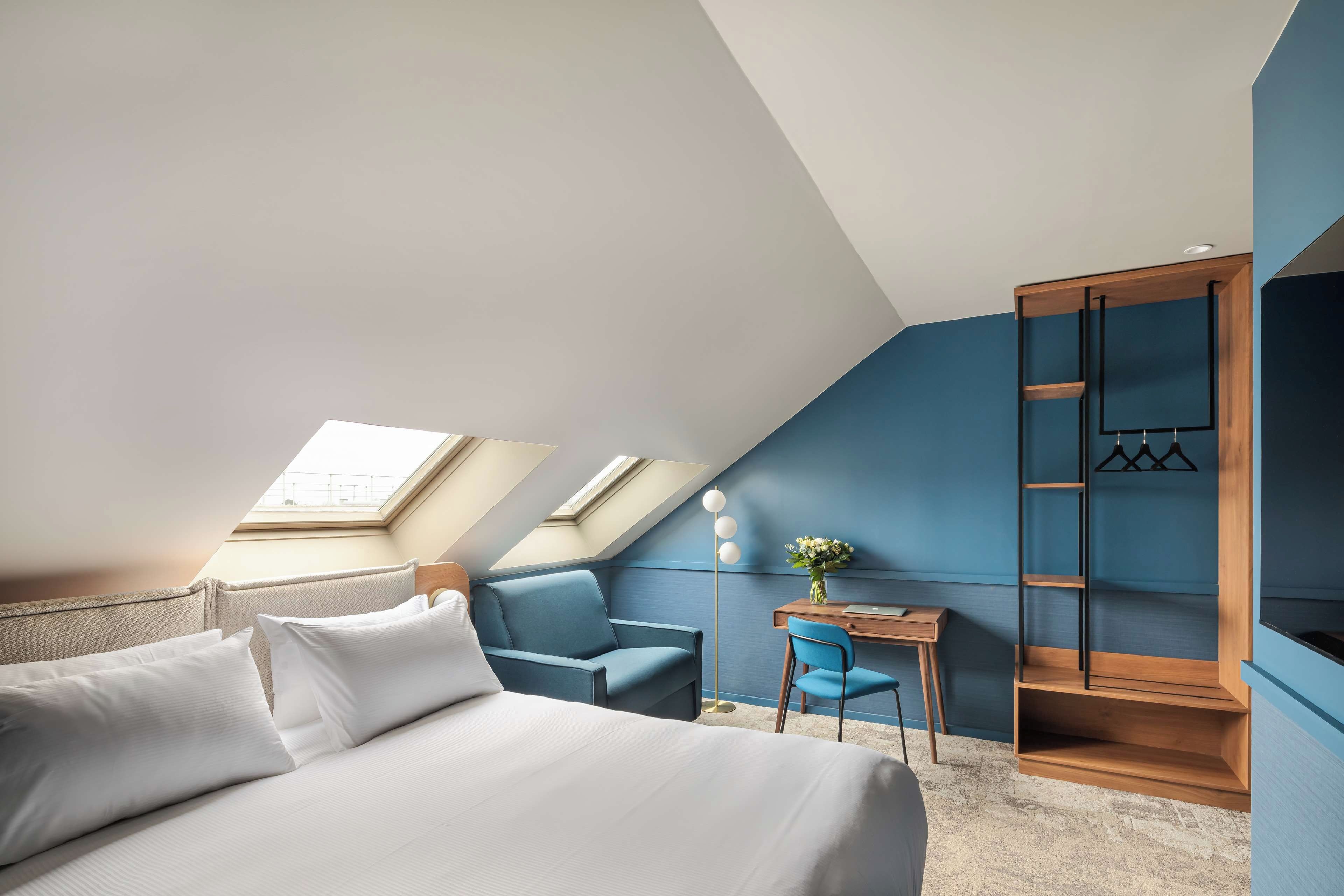 Un dormitorio moderno con techo inclinado, tragaluces, cama, escritorio, silla y armario.