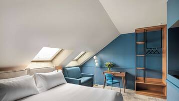 A modern bedroom with a sloped ceiling, skylights, a bed, a desk, a chair, and a wardrobe.