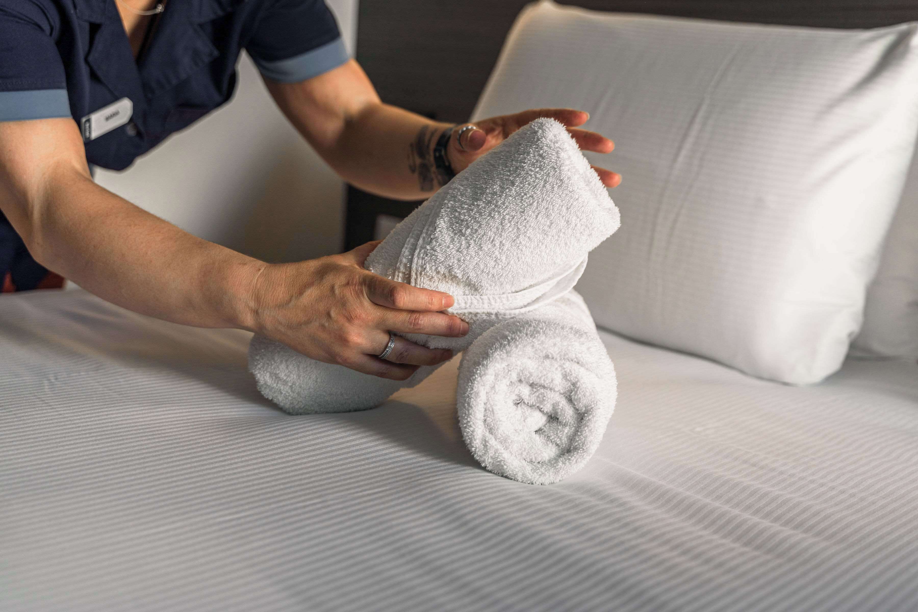 A person folding a white towel on a bed with a white pillow.