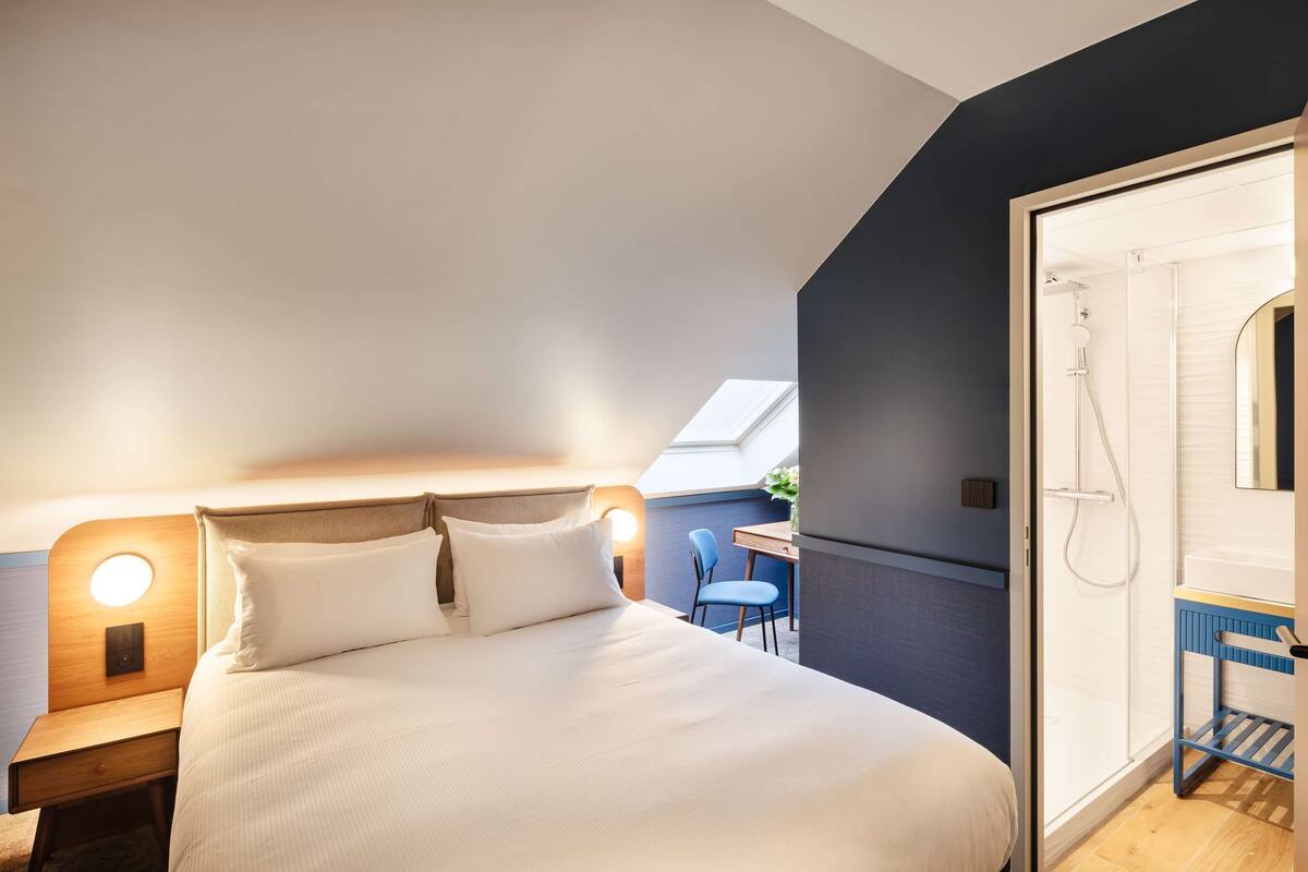 Een slaapkamer met een bed, nachtkastje en een klein bureau met stoel.