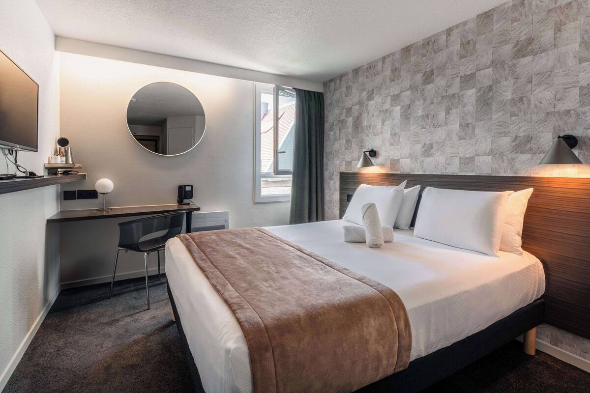Een hotelkamer met een bed, bureau, stoel en een grote spiegel.