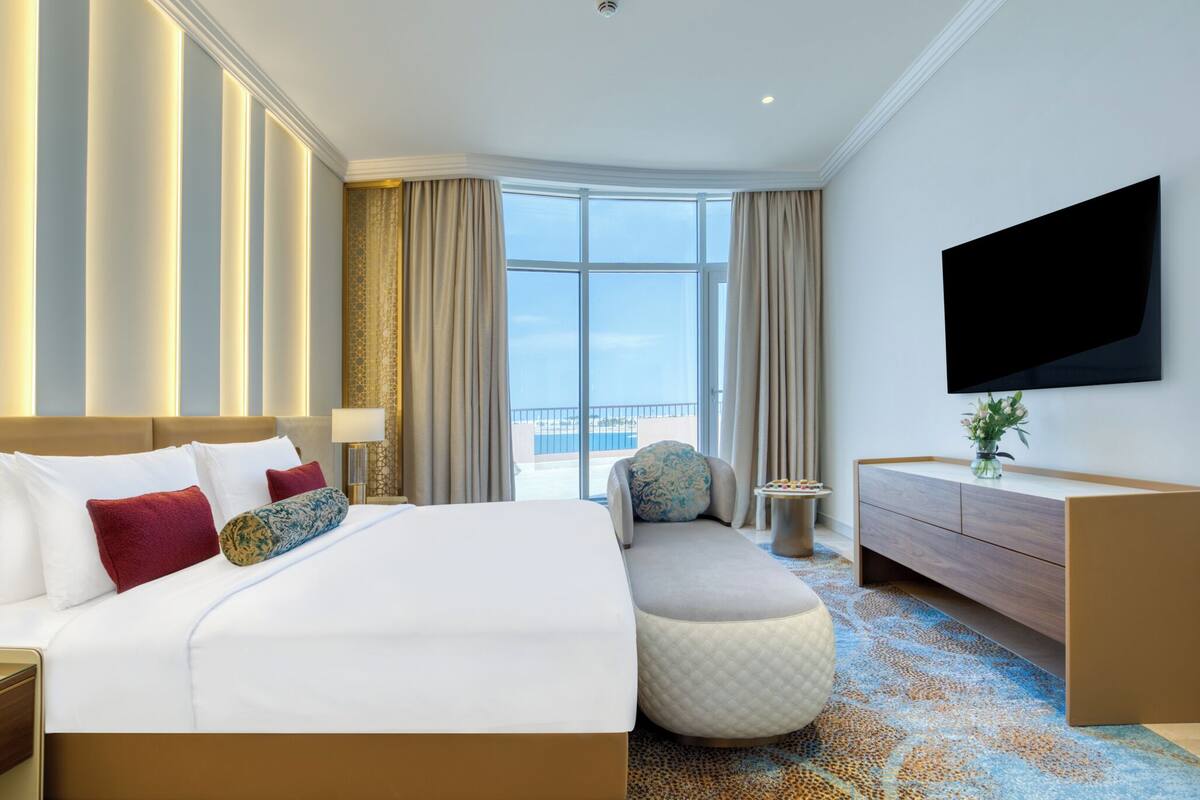 A hotel room with a large bed, a sofa, a TV, and a view of the city.