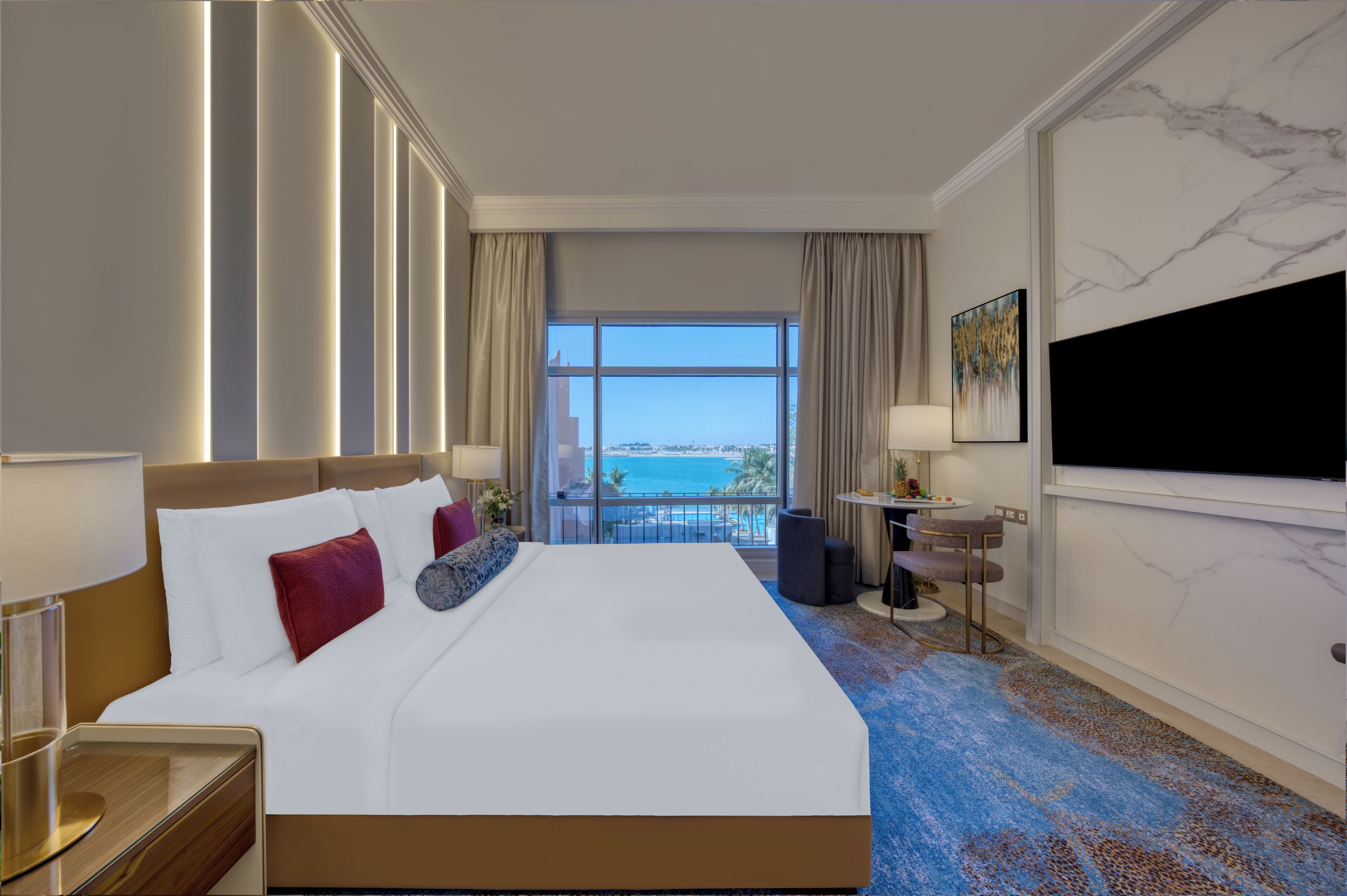 A hotel room with a large bed, a TV, a desk, and a view of the ocean.