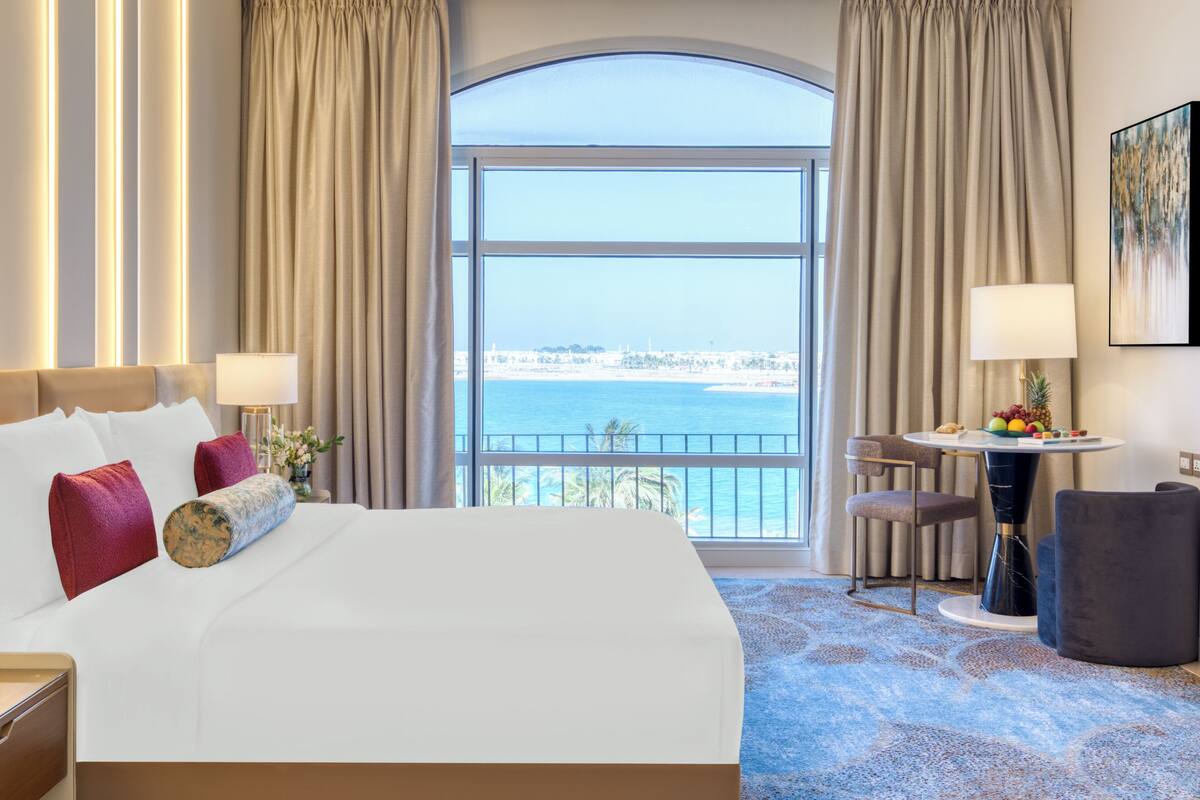 A hotel room with a large bed, a dining area, and a view of the sea.