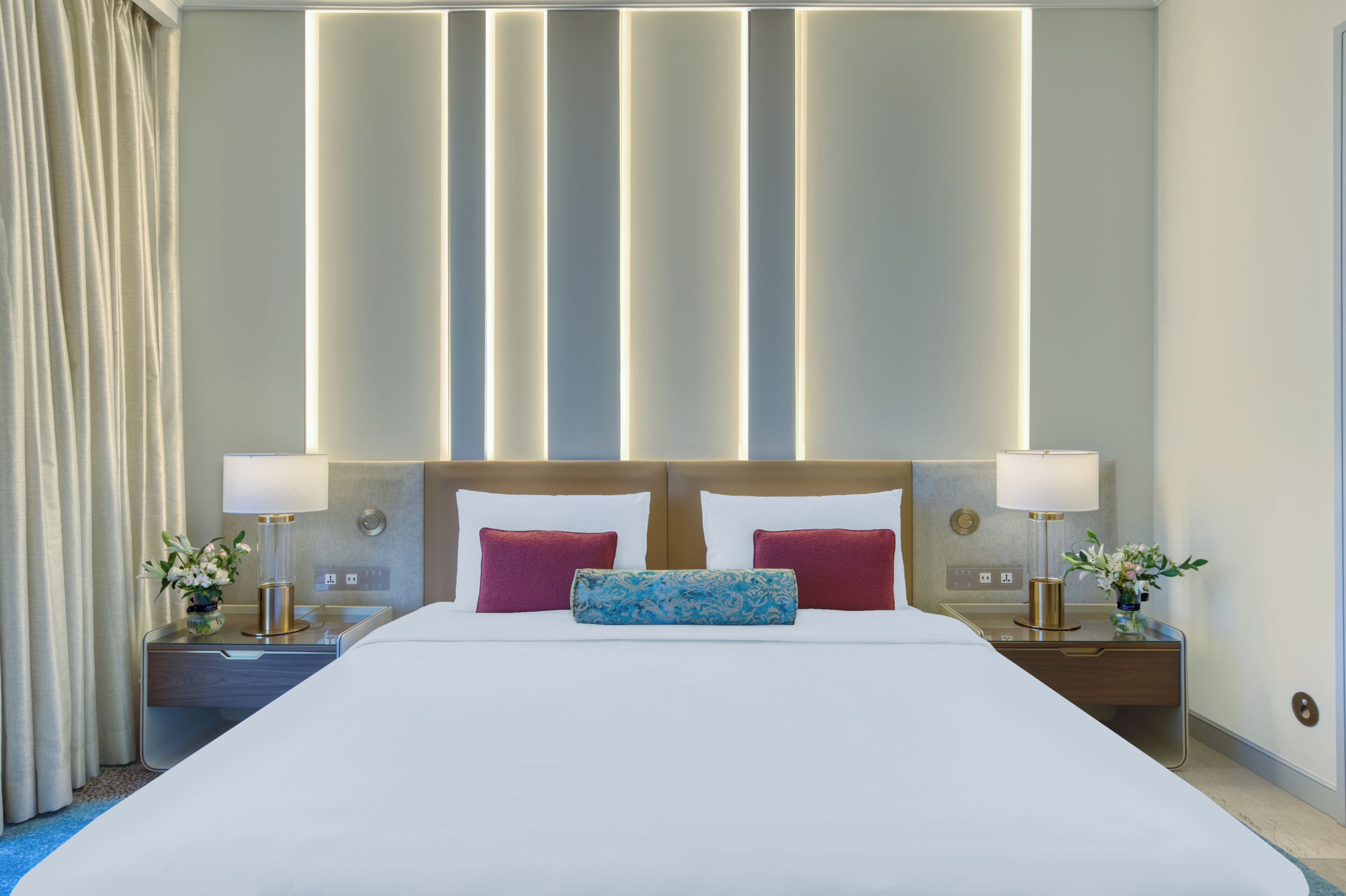 Habitación de hotel con una cama grande, dos mesitas de noche con lámparas y una pared con paneles de luz verticales.
