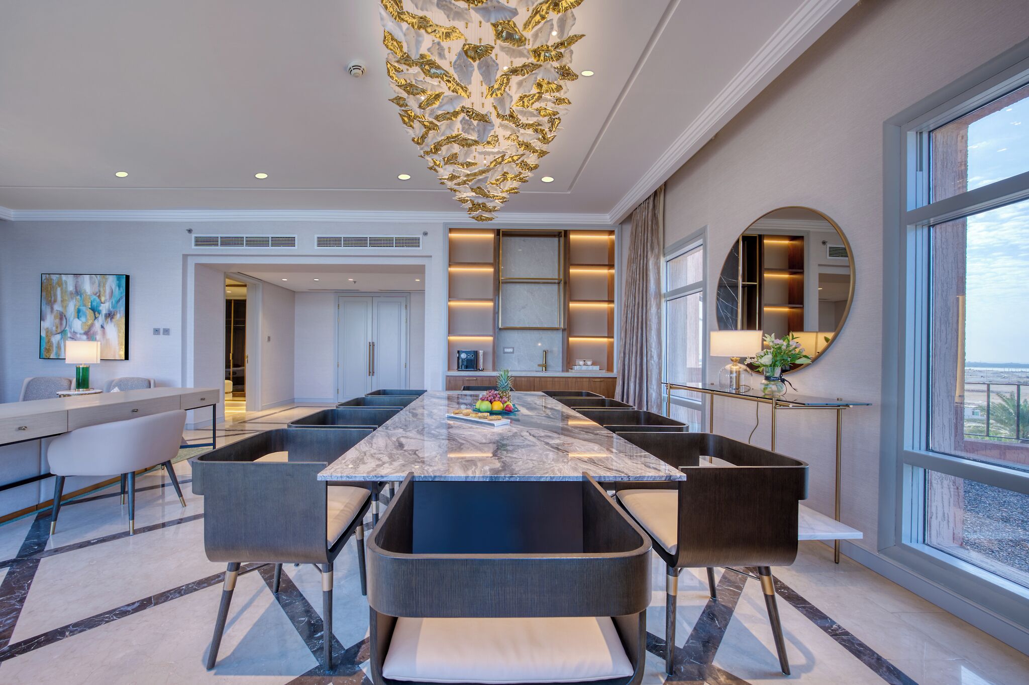 A modern kitchen with a marble island, built-in appliances, and a large window offering a view.