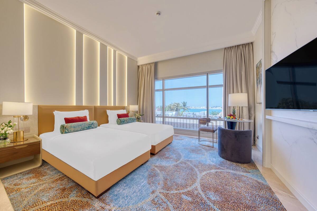 A hotel room with a large bed, a TV, a balcony with a view, and a desk with a lamp.