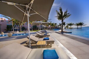 Una piscina al aire libre, sombrillas, sillones reclinables de piscina