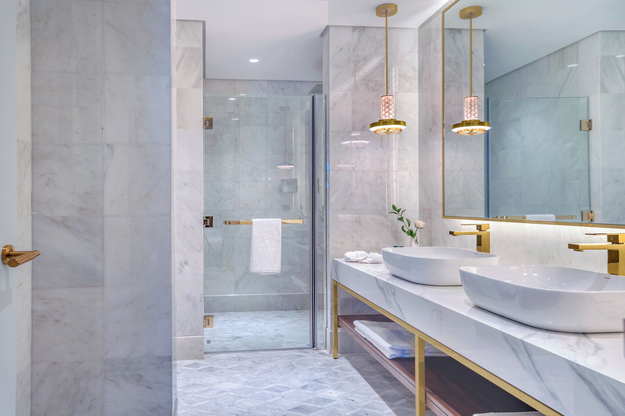 A modern bathroom with a glass shower enclosure, two sinks with gold fixtures, and a large mirror.