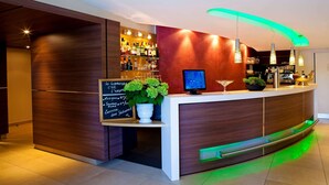 A modern reception desk with a wooden finish, a digital screen, and a potted plant. - Kyriad Nantes Sud Bouaye Aéroport (Bouaye)