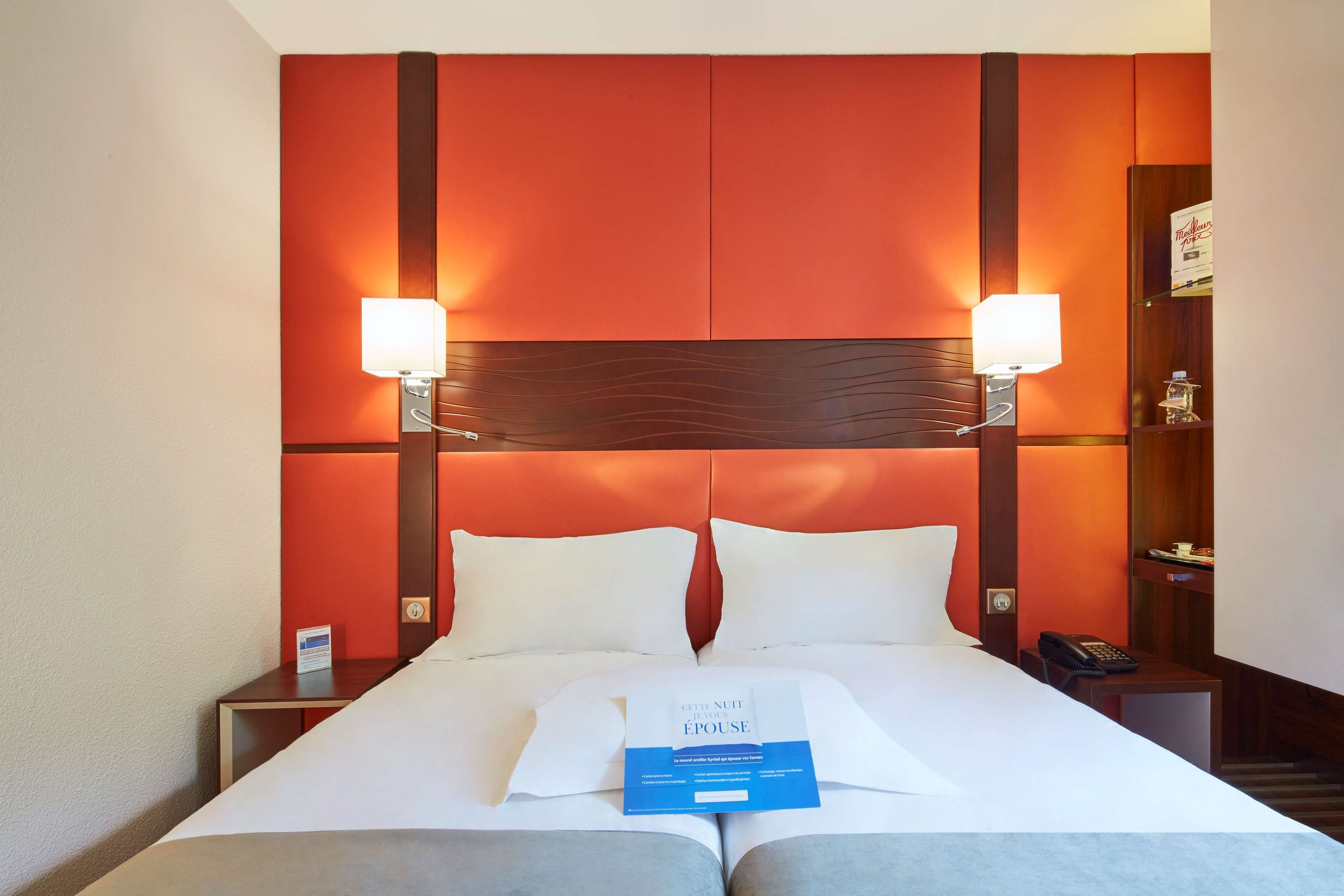 Quarto de hotel com uma cama grande, duas luminárias de cabeceira, mesa de cabeceira com telefone e um livro na cama.