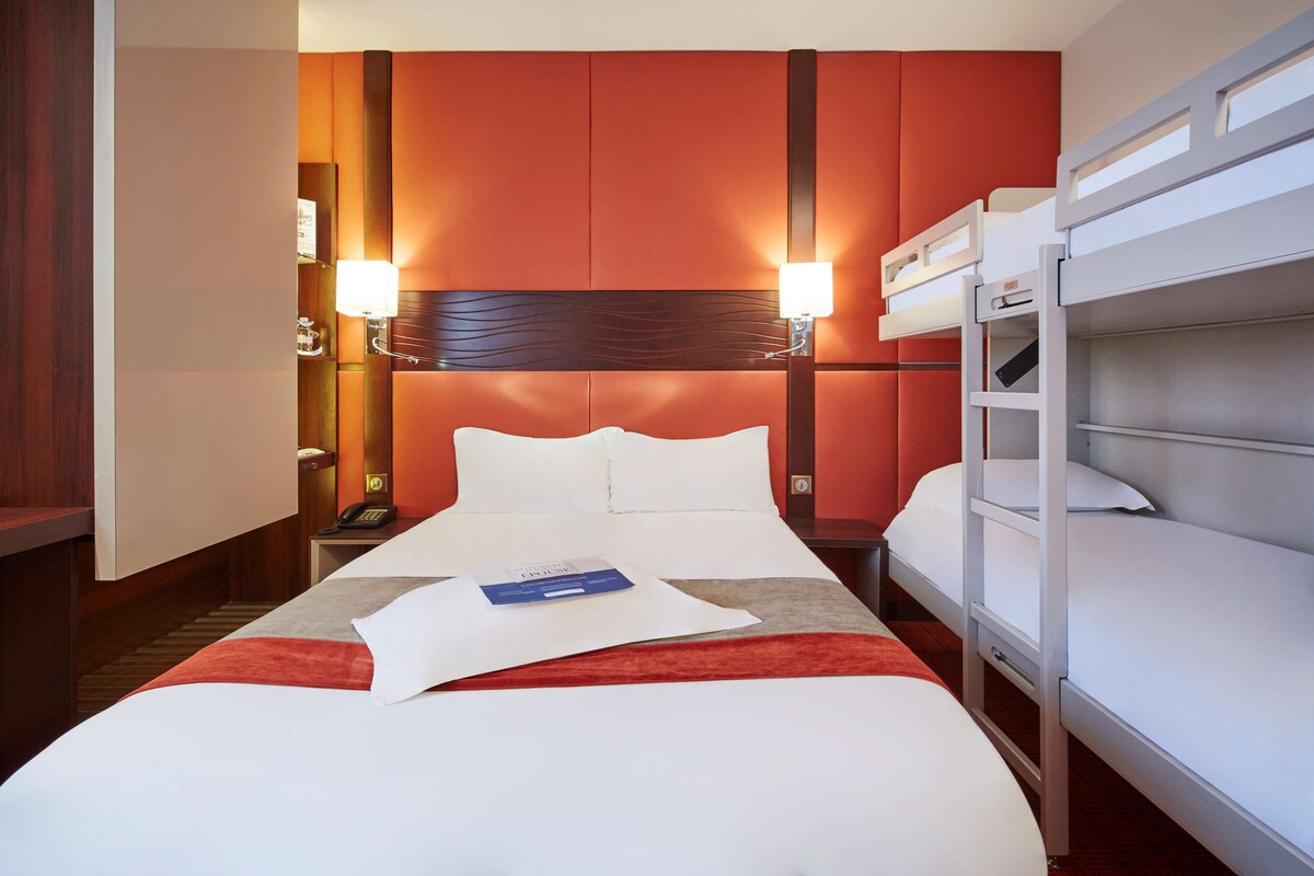 Una habitación de hotel con una cama grande, un escritorio con lámpara, un teléfono y una cama litera.