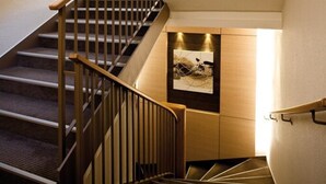 A staircase with wooden handrails and carpeted steps leading to a landing with a framed artwork. - Kyriad Nantes Sud Bouaye Aéroport (Bouaye)