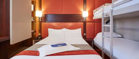 A hotel room with a bed, a bedside table, a lamp, a phone, and a bunk bed.