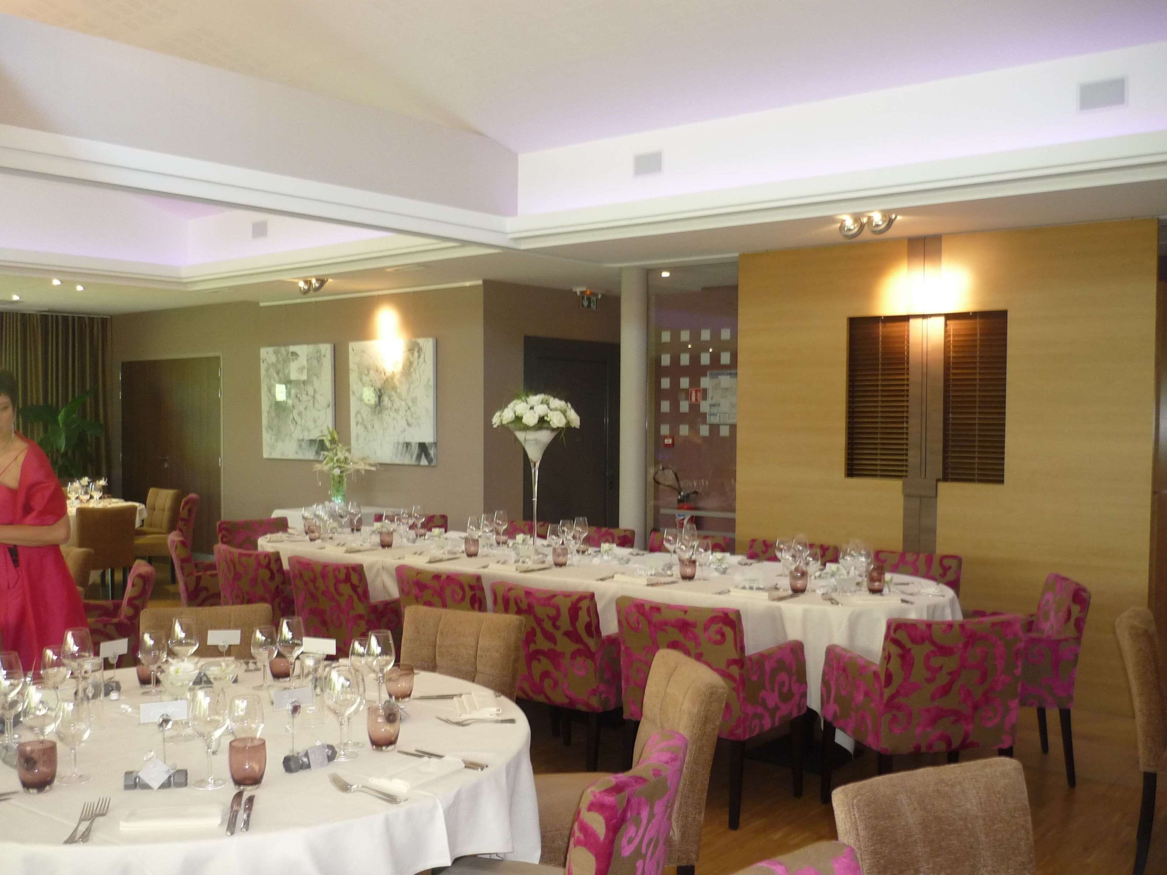 A dining area with round tables set for a meal, each with a white tablecloth and pink patterned chairs.