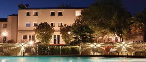 A building with a swimming pool, surrounded by palm trees and outdoor seating.