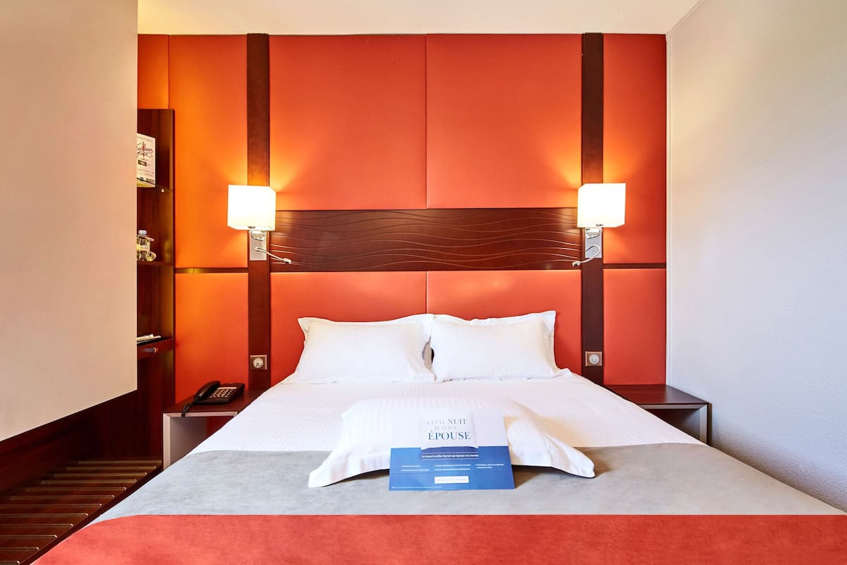 A hotel room with a large bed, two bedside lamps, a nightstand, and a telephone.