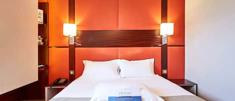 A hotel room with a large bed, two bedside lamps, a nightstand, and a telephone.