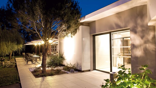 A modern building with a glass facade, outdoor seating area, and a well-lit garden. - Kyriad Nantes Sud Bouaye Aéroport (Bouaye)