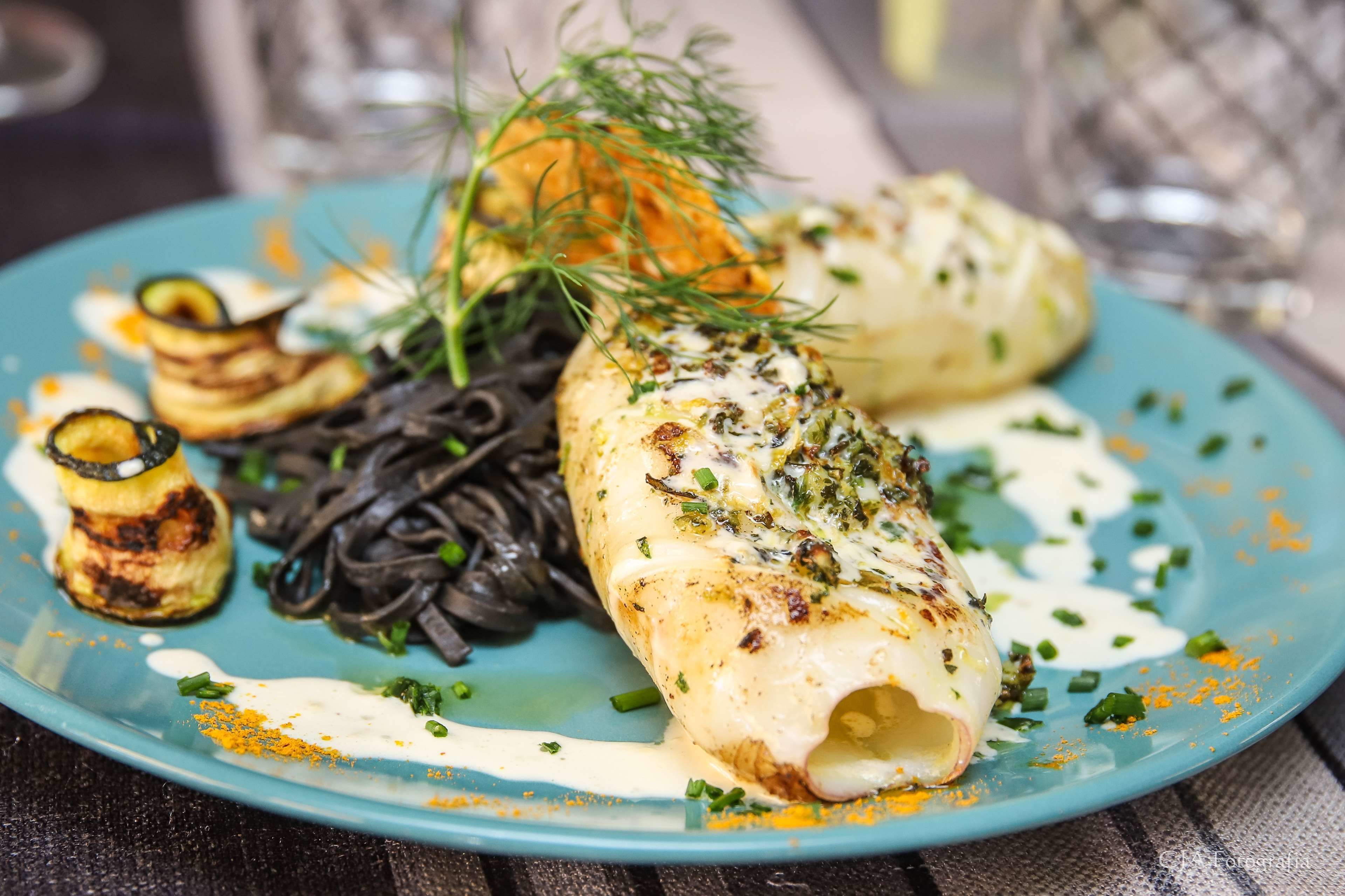 Un plato de comida con un borde azul, que incluye verduras a la parrilla, un relleno con hierbas y una salsa cremosa.
