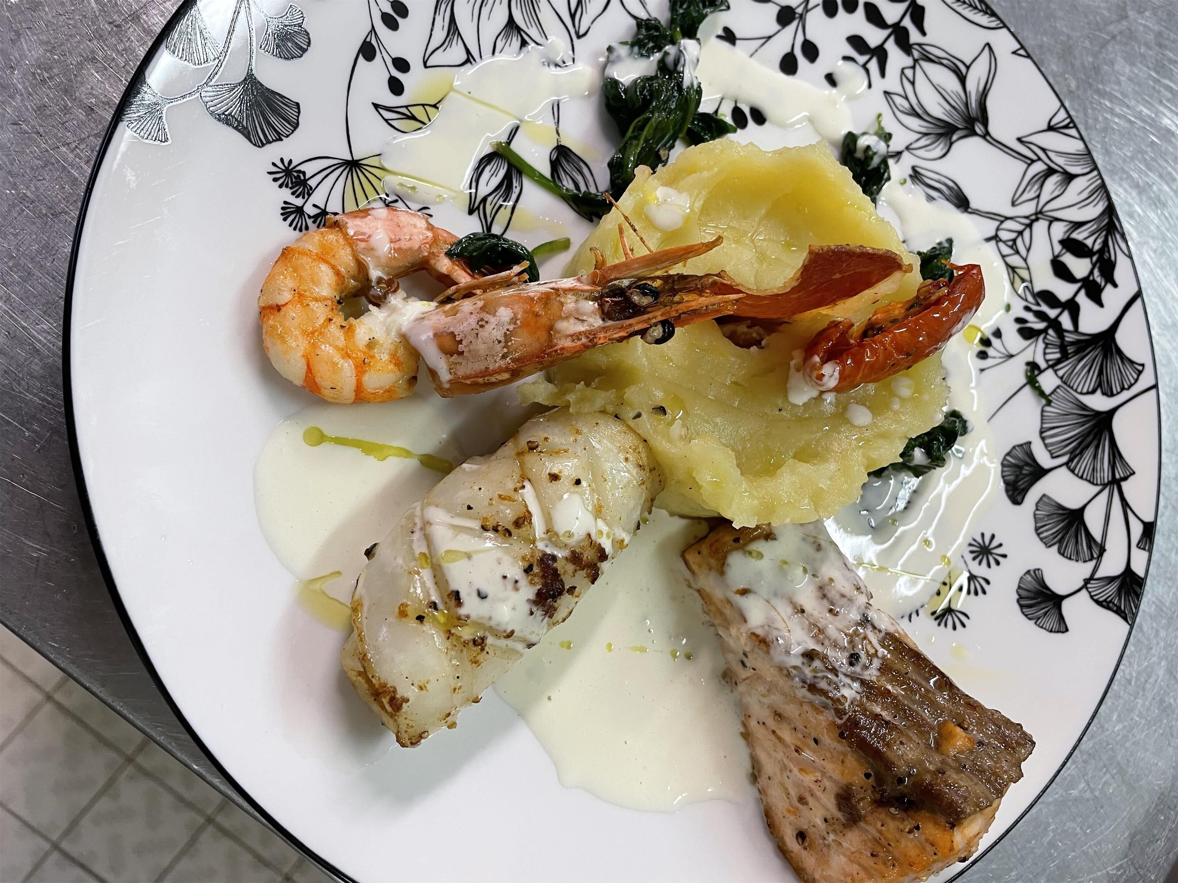 Une assiette de fruits de mer, comprenant des crevettes et du poisson, servie avec une sauce crémeuse et garnie d’herbes aromatiques.