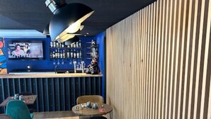 A restaurant interior with a bar area, wooden slat wall, and round tables.