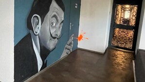 A hallway with a mural of a man holding a cigarette, a green exit sign, and a patterned door.