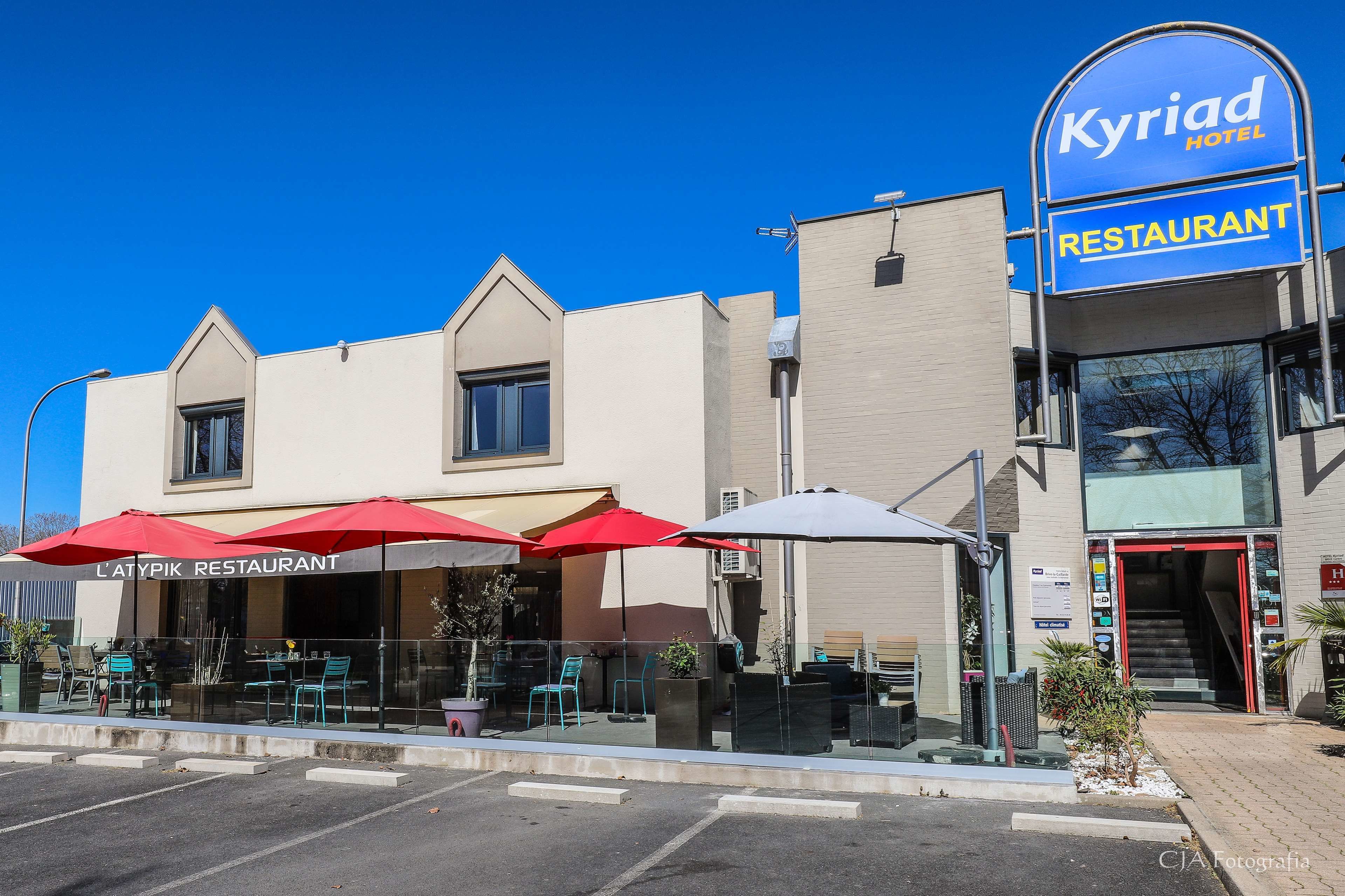 Un edificio con un restaurante llamado 'L'Atypik Restaurant' y la señalización del 'Kyriad Hotel'.